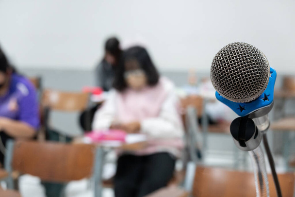 Zamknij mikrofon na stoliku wykładowcy w klasie z blure studentów jako tło. Zdjęcie edukacyjne. - Zdjęcie, obraz