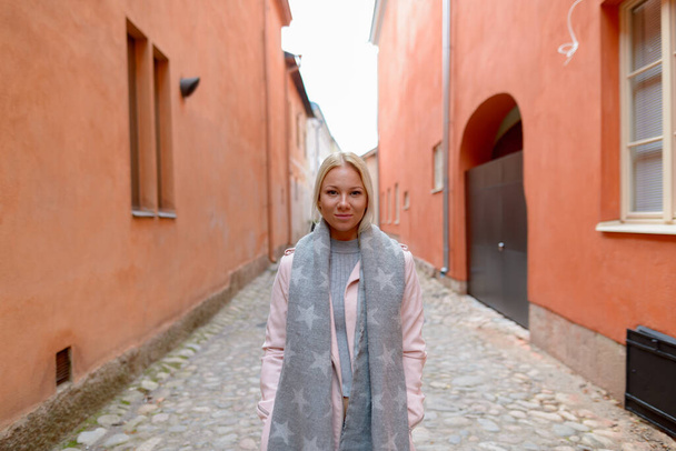 Portrét mladé krásné blondýny skandinávské ženy podél uličky s oranžovou budovou ve městě - Fotografie, Obrázek