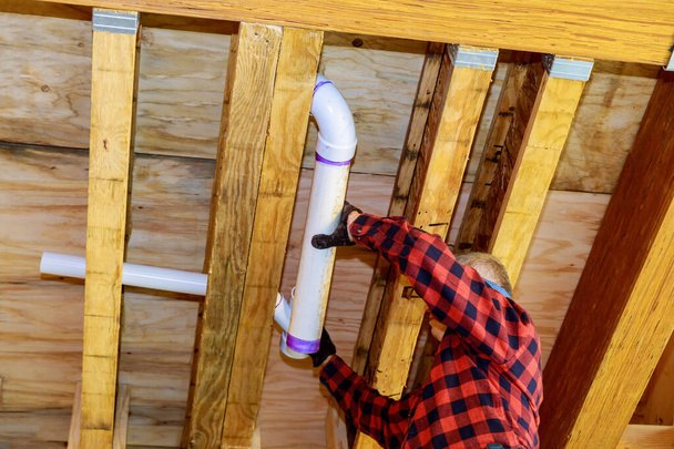 Tuyau blanc de toilette d'égout en plastique de PVC dans le collage de plombier, sur la poutre de plafond de cadre en bois de foyer doux de maison - Photo, image