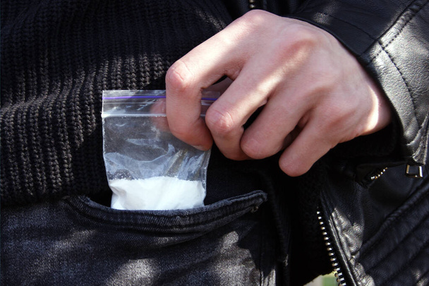 Un homme sort un sac en plastique d'une poche de jeans avec une dose de cocaïne ou un autre concept de drogue, de toxicomanie et de danger, de concentration sélective. - Photo, image
