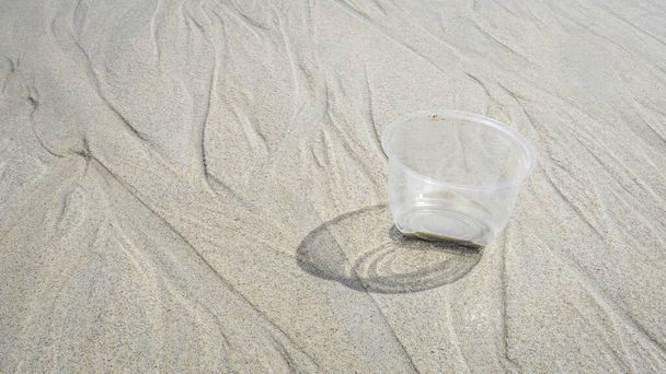 Transparente Plastikbecher am Strand verursachen Verschmutzung der Ozeane, für ein Umweltschutzkonzept. Müll an der Sandküste recyceln. - Foto, Bild