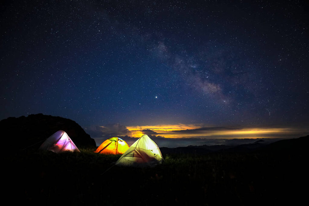 真夜中には美しい星空の下で3つのテントが立ち上がりました。夜の天の川の下のオレンジ色のテント. - 写真・画像