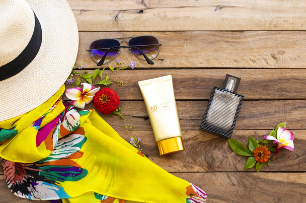 日焼け止めspf50化粧品帽子、サングラス、香水、黄色のスカーフ、ライフスタイルの花と肌の顔の健康管理女性は夏のアレンジメントでリラックス木製の背景にフラットレイスタイル - 写真・画像