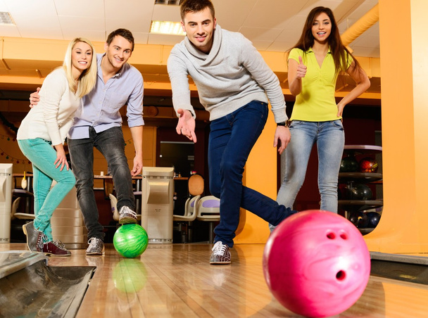 groep van vier jonge glimlachende mensen spelen bowling - Foto, afbeelding