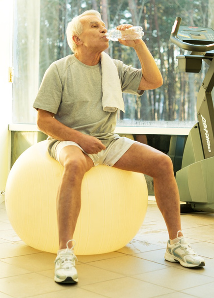 Втомлений старший чоловік з рушником і пляшкою води на фітнес-кулі
 - Фото, зображення