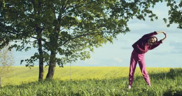 Молодая женщина греется на открытом воздухе в сельской замедленной съемке. Спортивная девушка занимается спортивным фитнесом на свежем воздухе природы в летний день копировального пространства. Концепция здорового образа жизни. - Кадры, видео