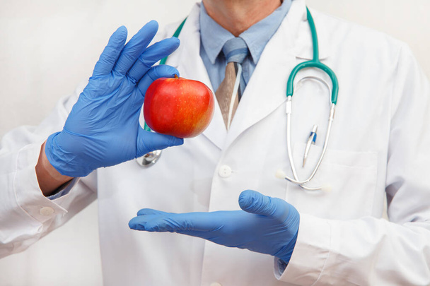 A doctor in protective gloves shows an apple as a concept of a healthy diet and lifestyle or proper nutrition. - Foto, Bild