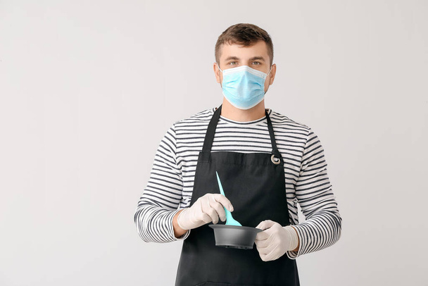 Мужчина парикмахер в медицинской маске на светлом фоне. Эпидемия коронавируса - Фото, изображение