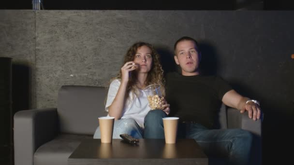 幸せなリラックスしたカップルはテレビで一緒に映画を見ながらポップコーンを食べる - 映像、動画