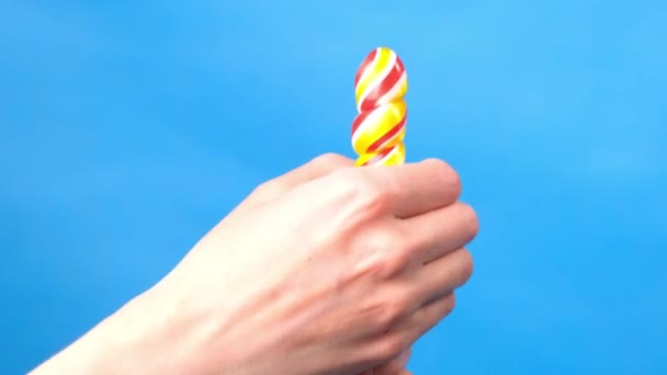 Close up of female hands. In a female hand a candy lollipop, on the other hand, a woman imitates masturbation. Blue simple background. - Footage, Video