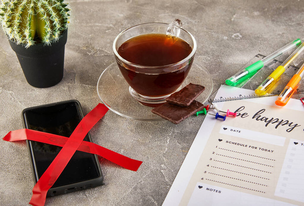 Concepto de desenchufe, teléfono móvil tachado con una cinta roja, café con chocolate y bolígrafos de colores, hojas de diario con una inscripción
 - Foto, Imagen