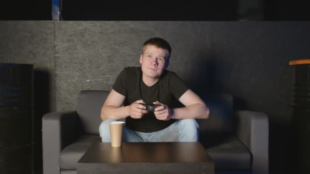 Молодой человек играет в консольную игру перед камерой, побеждая своего оппонента онлайн. Белый человек на диване. - Кадры, видео