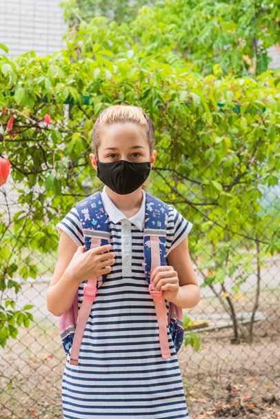 Школьная девочка в черной защитной маске с рюкзаком. Школьница в школьной форме. Падение. Скоро вернусь в школу.. - Фото, изображение