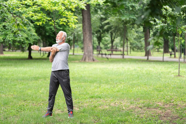Senior sportsman doing stretching exercise at park, healthy lifestyle concept - Фото, изображение