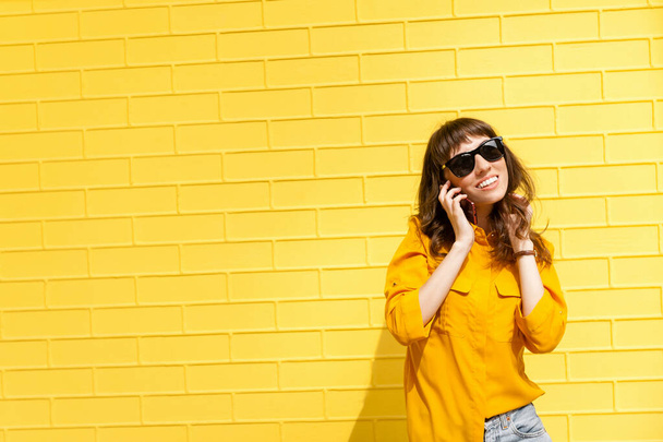 Meisje aan de telefoon kreeg het blijde nieuws... meisje in geel shirt tegen de gele muur, aan de telefoon aan het praten. Kopieerruimte - Foto, afbeelding