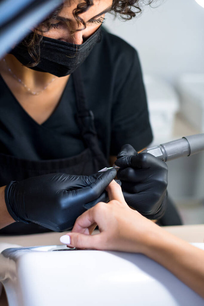 manicurist master in black gloves and mask is making manicure with a manicure drill apparatus - Foto, Imagem