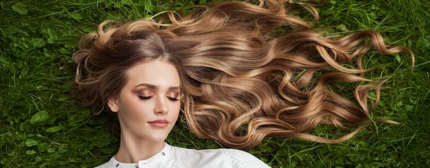 Mulher bonita com cabelo encaracolado saudável relaxante na grama verde ao ar livre, vista superior
 - Foto, Imagem