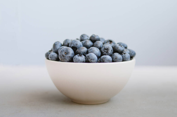 Foto minimalista de arándanos recién recogidos en un tazón blanco sobre fondo azul oscuro. puñado de bayas maduras dulces de cerca  - Foto, imagen