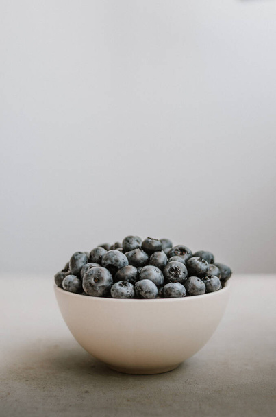 Freshly picked blueberry in white bowl on dark blue background. Handful of sweet ripe berries close up  - Photo, Image