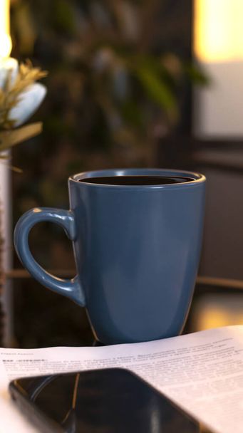 Evening coffee. Blue cup with coffee, open book and mobile phone, evening light, sunset, dusk. Atmospheric, cozy evening in the garden, green leaves, conversation. Warm light, blur bokeh. - Foto, Bild