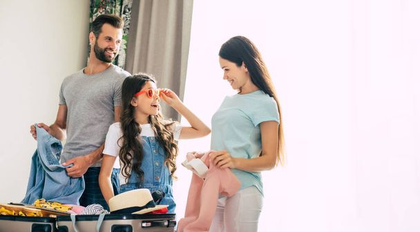 Beautiful young happy and excited family in a luxury hotel room while unpacking stuff and clothes and having fun together. Vacation or trip in summer - Foto, imagen