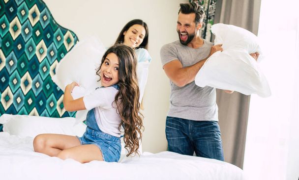 Funny and excited family are having fun, jumping and playing together on the bed in a big room - Foto, imagen