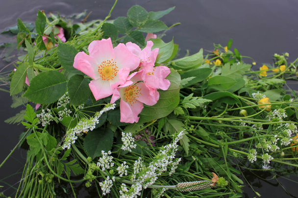 Fiori di mezza estate sull'acqua. Mazzo di rosa canina, ranuncoli gialli e fiori selvatici sul fiume nella notte di Ivana Kupala. - Foto, immagini