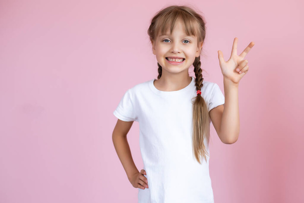 Beautiful little blonde girl with long hair in white T-shirt smiling on a pink background - 写真・画像