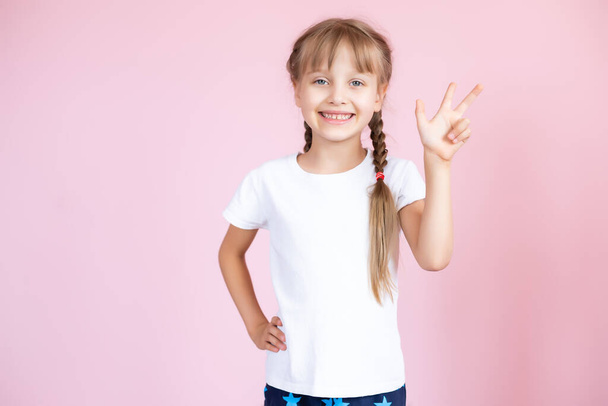 Schöne kleine blonde Mädchen mit langen Haaren in weißem T-Shirt lächelnd auf einem rosa Hintergrund - Foto, Bild