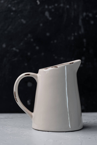 Alte Keramikkanne auf grauer Oberfläche. Schwarzer Hintergrund. - Foto, Bild