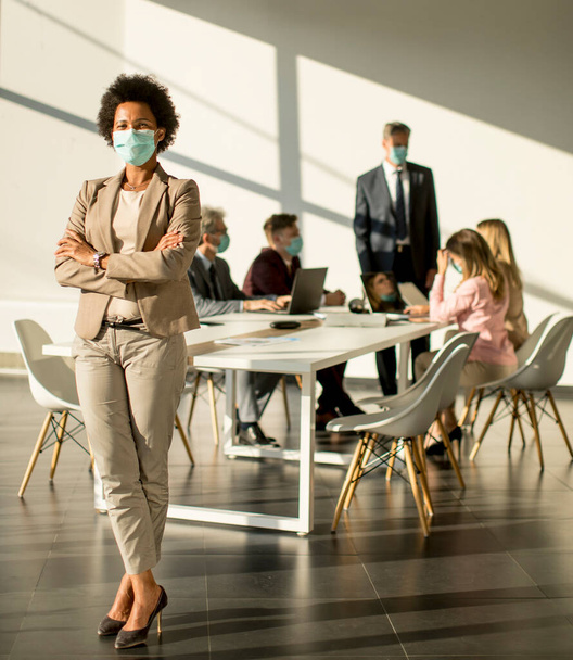 Afro-Amerikaanse vrouw in het kantoor voor haar team en draag masker als bescherming tegen corona virus - Foto, afbeelding