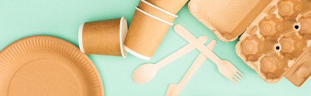 Horizontal crop of disposable tableware and wooden cutlery on green background, ecology concept - Photo, Image