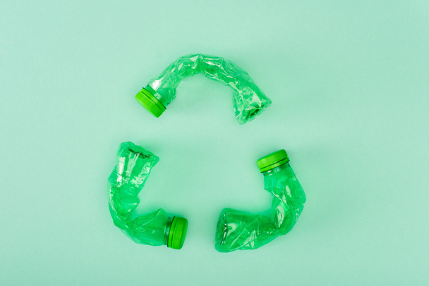 Vista superior del signo de reciclaje de botellas de plástico arrugadas sobre fondo verde, concepto de ecología - Foto, Imagen