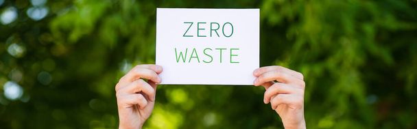 Horizontal crop of man holding card with zero waste lettering outdoors, ecology concept - 写真・画像