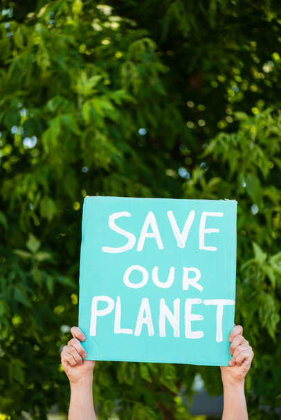 Καλλιεργημένη άποψη του ανθρώπου κρατώντας πλακάτ με σώσει τον πλανήτη μας γράμματα με δέντρα στο παρασκήνιο, έννοια οικολογία - Φωτογραφία, εικόνα