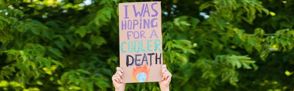 Panoramic orientation of man holding placard with i was hoping for a cooler death lettering with trees at background, ecology concept  - Фото, зображення