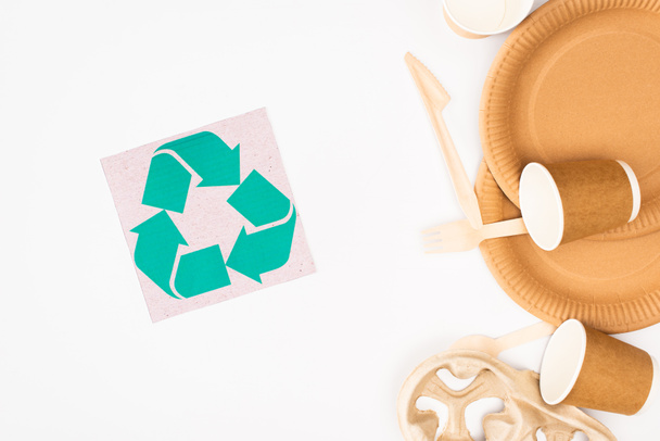 Vista superior de la tarjeta con signo de reciclaje y vajilla desechable y cubiertos de madera sobre fondo blanco, concepto de ecología - Foto, imagen
