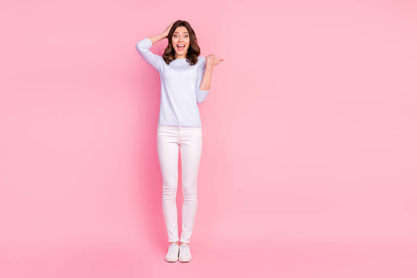 Full size photo of attractive shocked lady good mood directing finger empty space showing novelty product wear casual white pullover trousers sneakers isolated pink color background - Foto, Bild