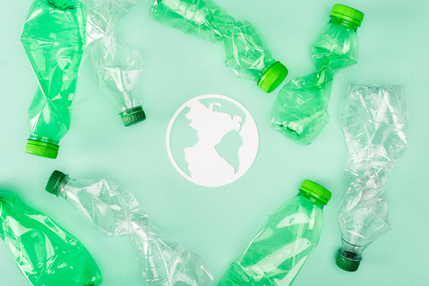 Widok góry papieru planeta znak w pobliżu pogniecionych butelek plastikowych na zielonej powierzchni, koncepcja ekologia - Zdjęcie, obraz