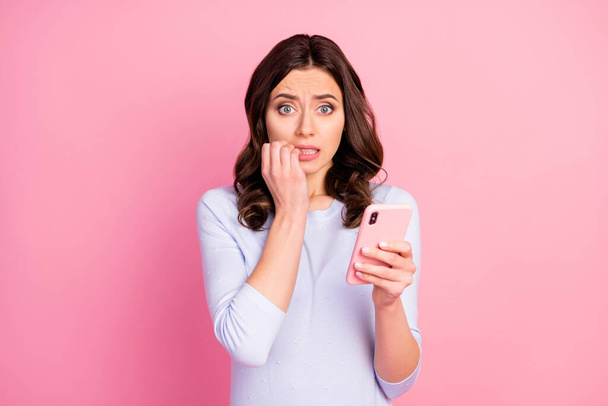 Photo of beautiful terrified lady hold telephone quarantine time read news corona virus infection spreading bite fingers fear wear casual white shirt isolated pastel pink color background - Photo, Image