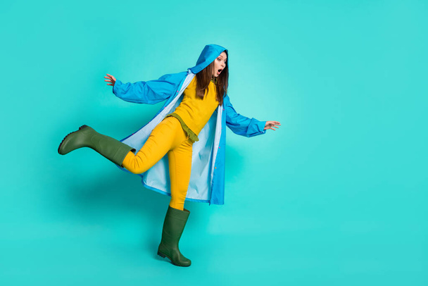 Full body photo of attractive terrified lady rainy weather street walk hood on head many puddles falling slippery road wear raincoat sweater pants gum boots isolated teal color background - Foto, immagini