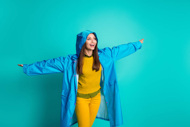 Photo of attractive funny lady cheerful mood spread arms like wings rainy weather street walk rejoicing wear casual outfit raincoat hood isolated teal color background - Foto, Imagem
