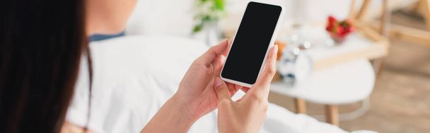 Horizontal crop of woman holding smartphone with blank screen on bed - Foto, imagen
