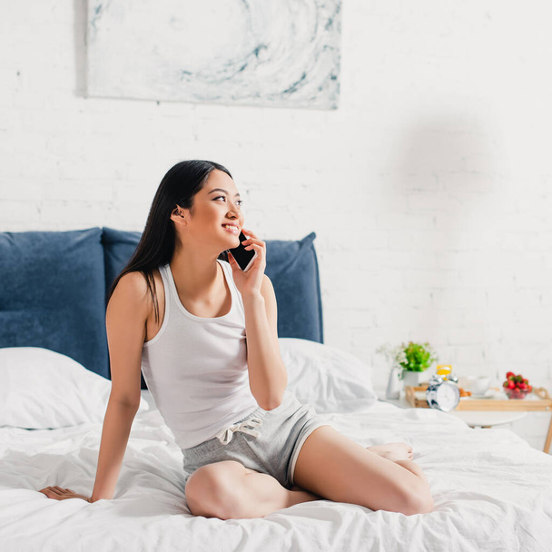 Красива азіатська дівчина розмовляє на смартфоні в ліжку вранці
  - Фото, зображення