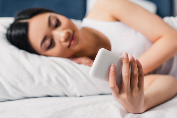 Selective focus of asian woman using smartphone on bed  - Fotó, kép