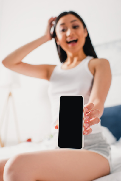 Selective focus of positive asian woman showing smartphone with blank screen on bed  - Foto, Imagem