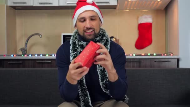 Homem de Papai Noel chapéu, pega caixa vermelha com presente em mãos, examina, sorri
 - Filmagem, Vídeo