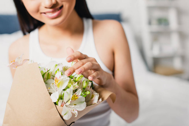 Cropped view of smiling woman touching flowers in bouquet on bed - Foto, afbeelding