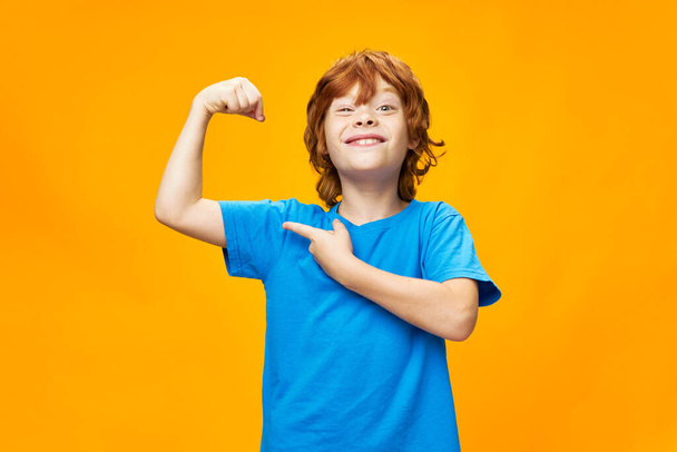 strong red-haired boy in a blue t-shirt on a yellow background  - Photo, Image