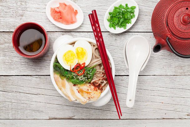 Asijská nudlová ramenová polévka s kuřecím masem, zeleninou a vejci a bylinkovým čajem na dřevěném pozadí. Horní pohled rovný - Fotografie, Obrázek